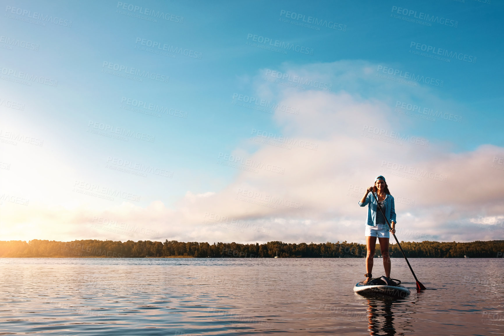 Buy stock photo Shot of a young woman paddle boarding on a lake