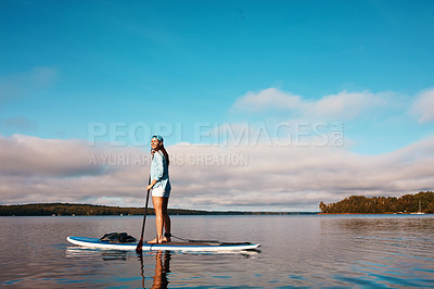 Buy stock photo Shot of a young woman paddle boarding on a lake