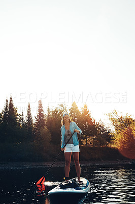 Buy stock photo Shot of a young woman paddle boarding on a lake