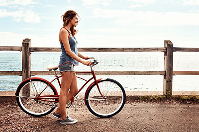 Buy stock photo Shot of a beautiful young woman with her bicycle on the promenade