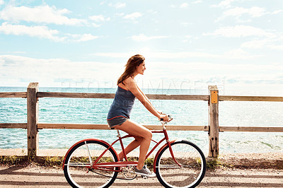 Buy stock photo Shot of a beautiful young woman riding her bicycle on the promenade