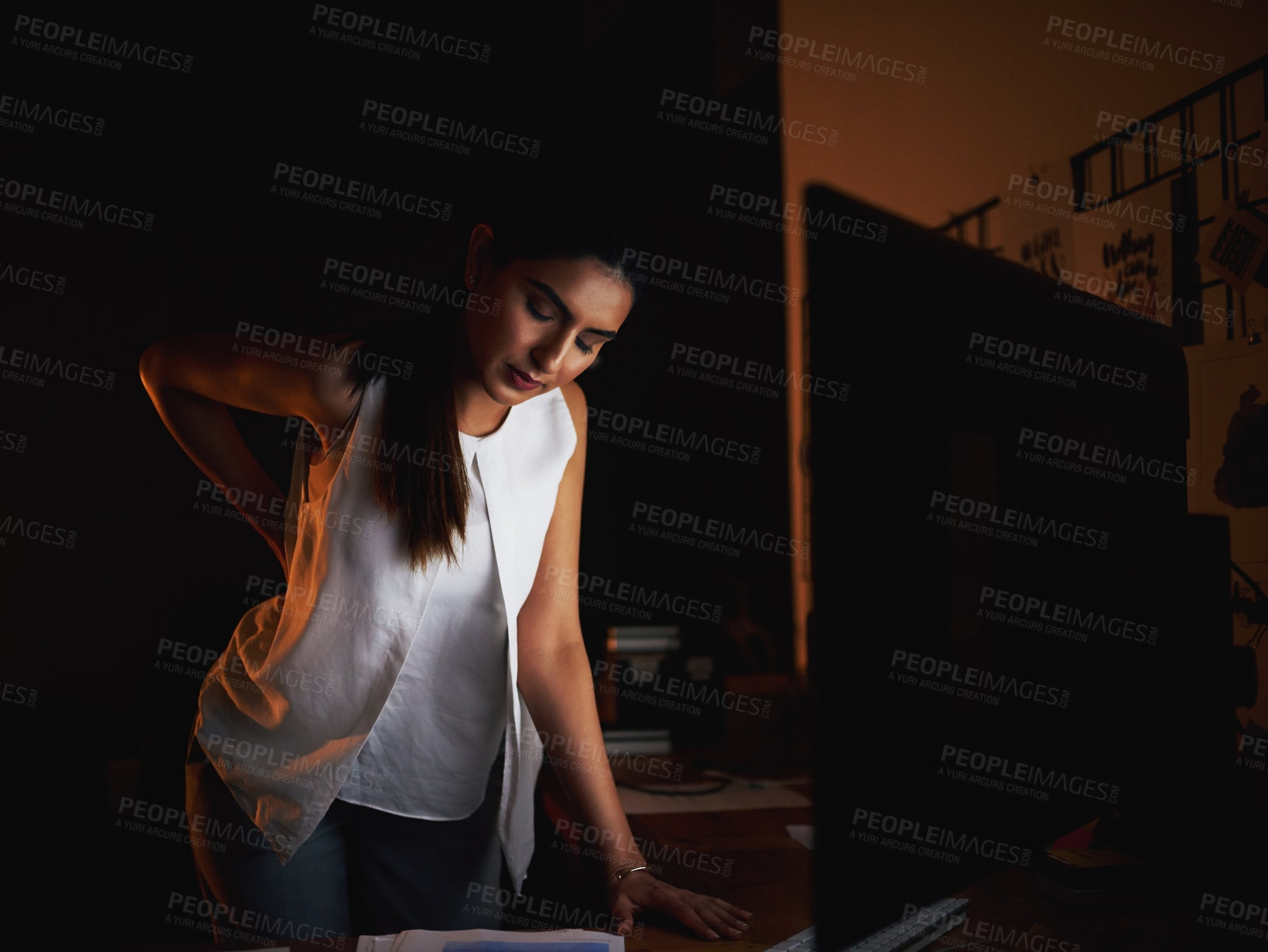 Buy stock photo Shot of a young businesswoman suffering with back pain while working late in an office