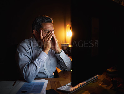 Buy stock photo Shot of a mature businessman looking stressed out while working late in an office