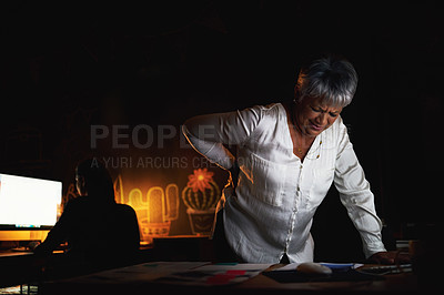 Buy stock photo Shot of a mature businesswoman suffering with back pain while working late in an office