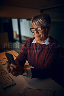 Buy stock photo Shot of a mature businesswoman using a cellphone while working late in an office