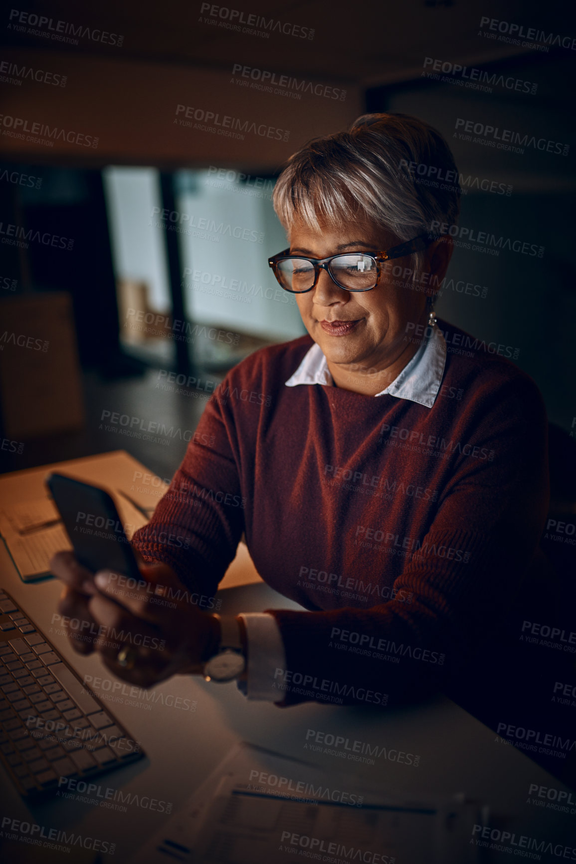 Buy stock photo Shot of a mature businesswoman using a cellphone while working late in an office