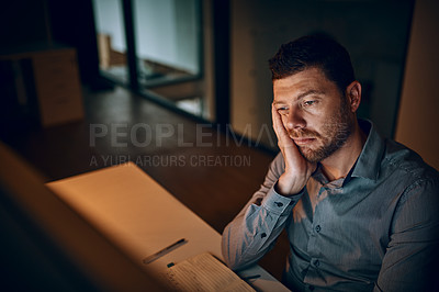 Buy stock photo Shot of a young businessman looking bored while working late in an office