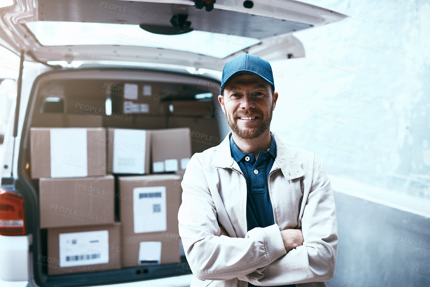 Buy stock photo Portrait of a cheerful young delivery man standing next to a van full of boxes with his arms folded outside during the day