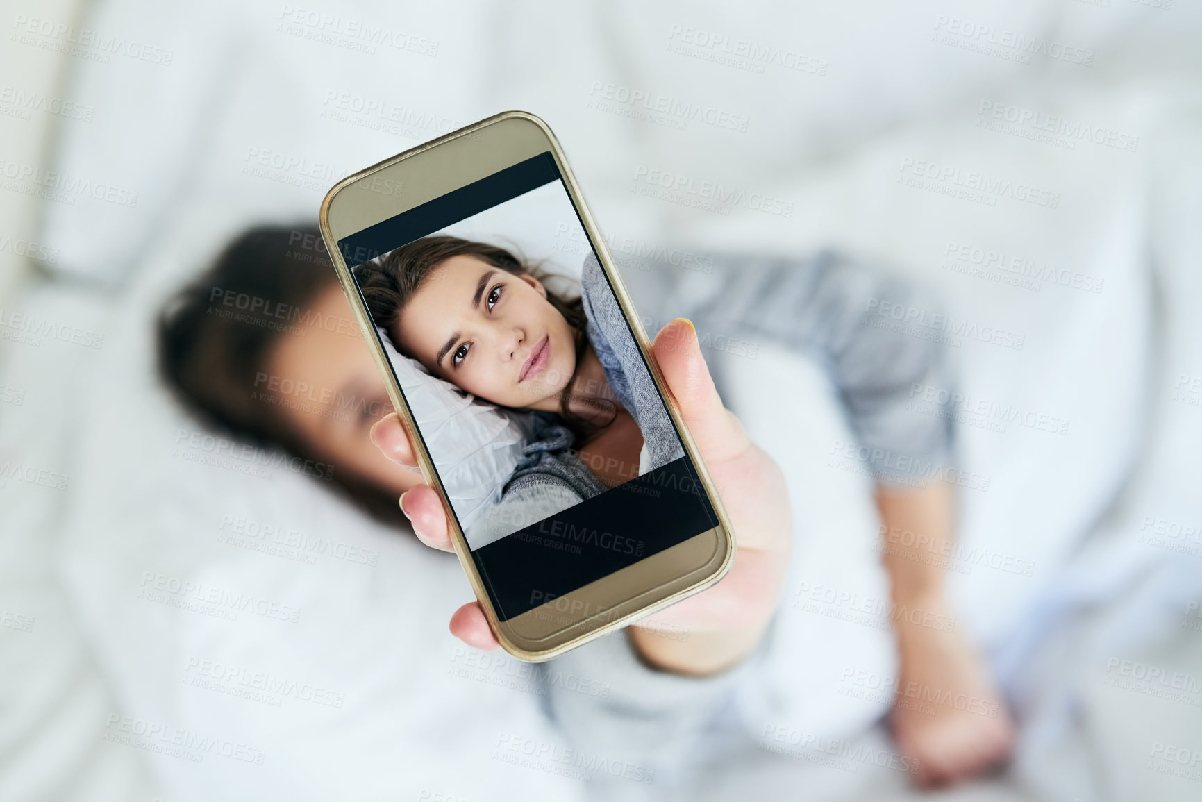 Buy stock photo Shot of an attractive young woman taking a self portrait with her cellphone while lying in bed at home
