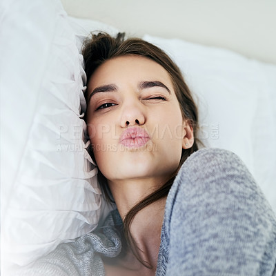 Buy stock photo Portrait of an attractive young woman blowing a kiss while lying in bed at home during the day