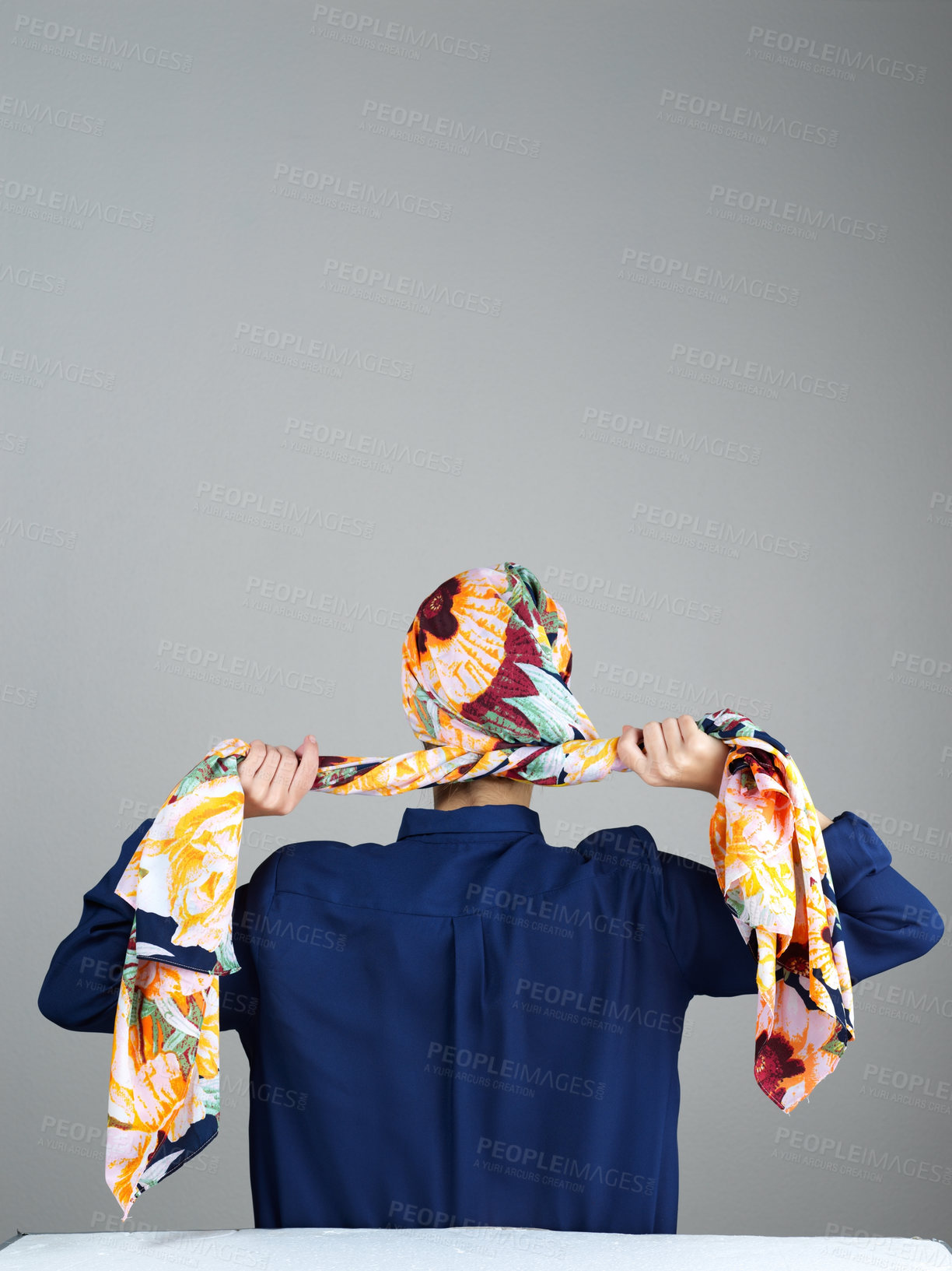 Buy stock photo Rearview studio shot of  an unrecognizable woman wearing a head scarf and tying it up while standing against a grey background