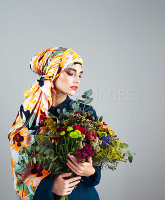 Buy stock photo Studio shot of a confident young woman wearing a colorful head scarf and holding a bouquet of flowers against a grey background