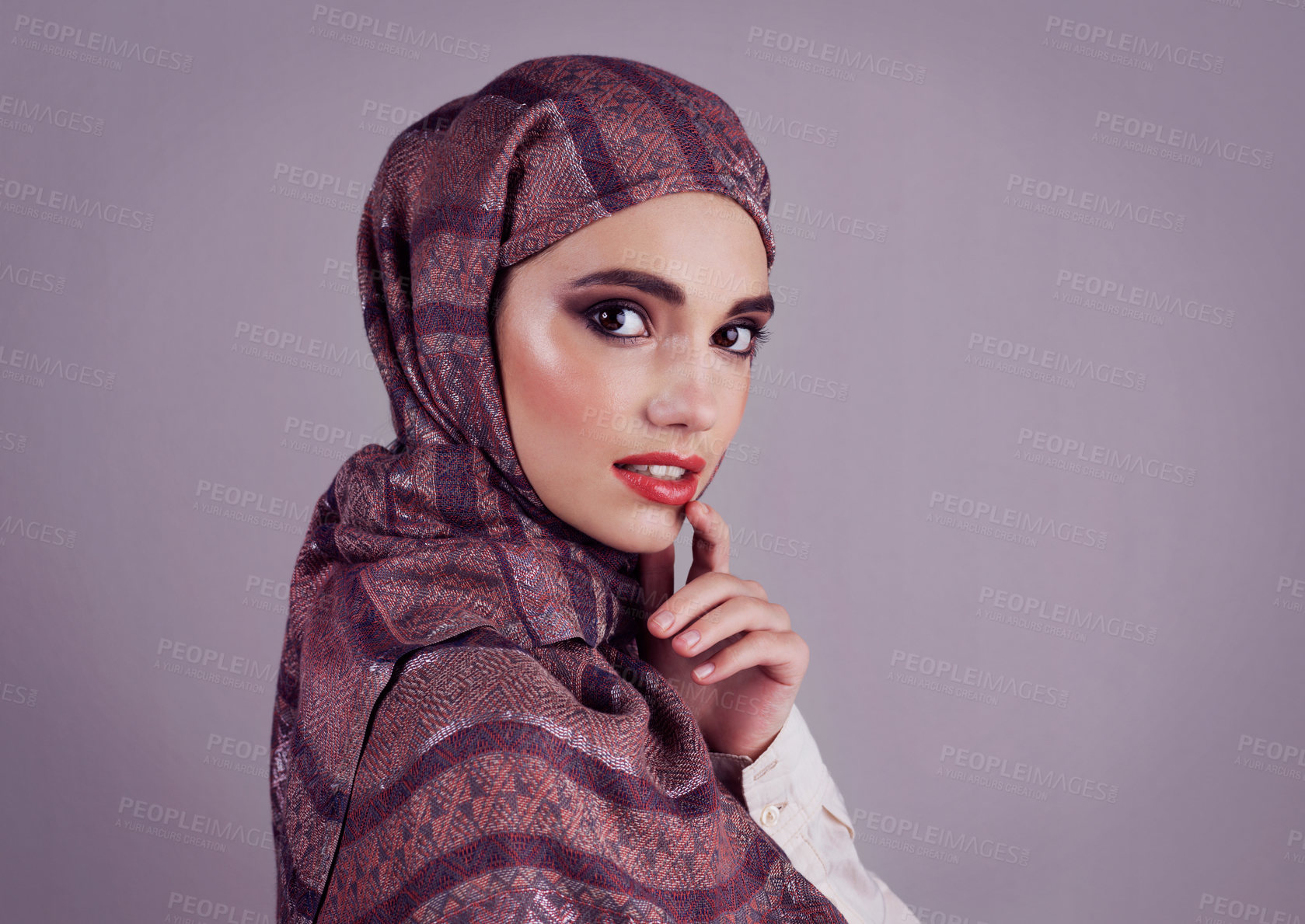 Buy stock photo Studio portrait of a confident young woman wearing a colorful head scarf while applying red lipstick to her lips