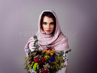 Buy stock photo Studio portrait of a confident young woman wearing a colorful head scarf and holding a bouquet of flowers against a grey background