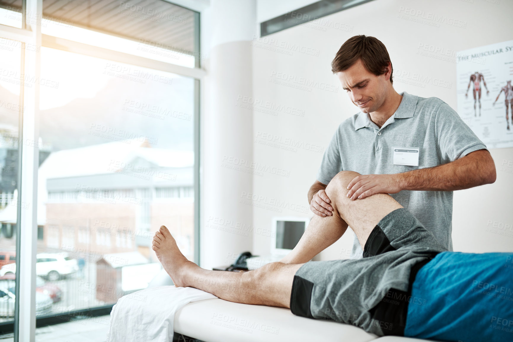 Buy stock photo Shot of a young male physiotherapist helping a client with leg exercises who's lying on a bed
