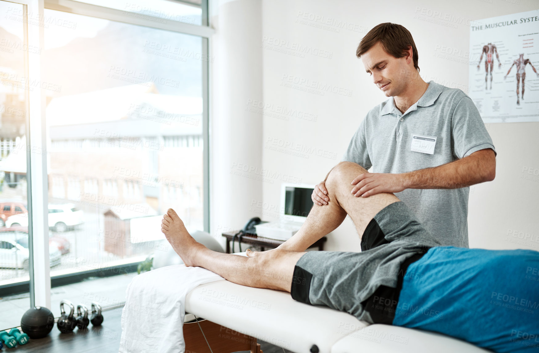 Buy stock photo Shot of a young male physiotherapist helping a client with leg exercises who's lying on a bed