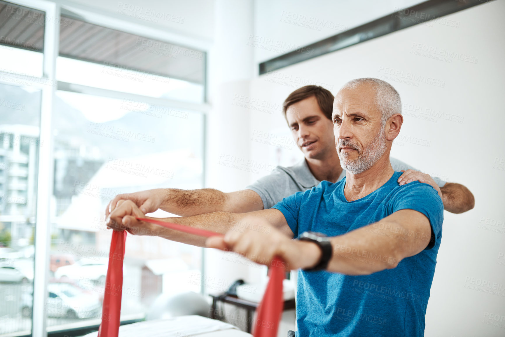 Buy stock photo Shot of a young male physiotherapist helping a client with stretching exercises in his office during the day