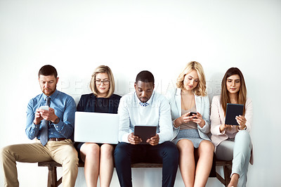 Buy stock photo Shot of a group of work colleagues seated next to each other while using electronic devices against a white background