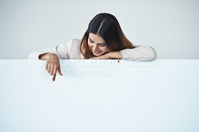 Buy stock photo Studio shot of an attractive young businesswoman pointing at copy space on a blank placard