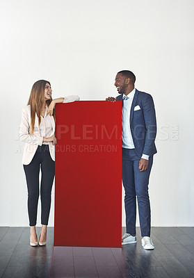 Buy stock photo Studio shot of a young businessman and businesswoman standing next to a blank red placard