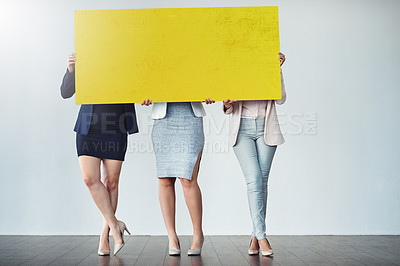 Buy stock photo Studio shot of a group of businesswomen holding up a blank yellow placard in front of them