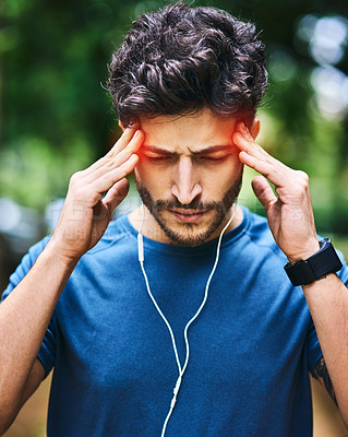 Buy stock photo Shot of a sporty young man suffering with a headache while exercising outdoors
