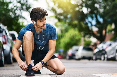 Buy stock photo Shot of a sporty young man tying his shoelaces while exercising outdoors