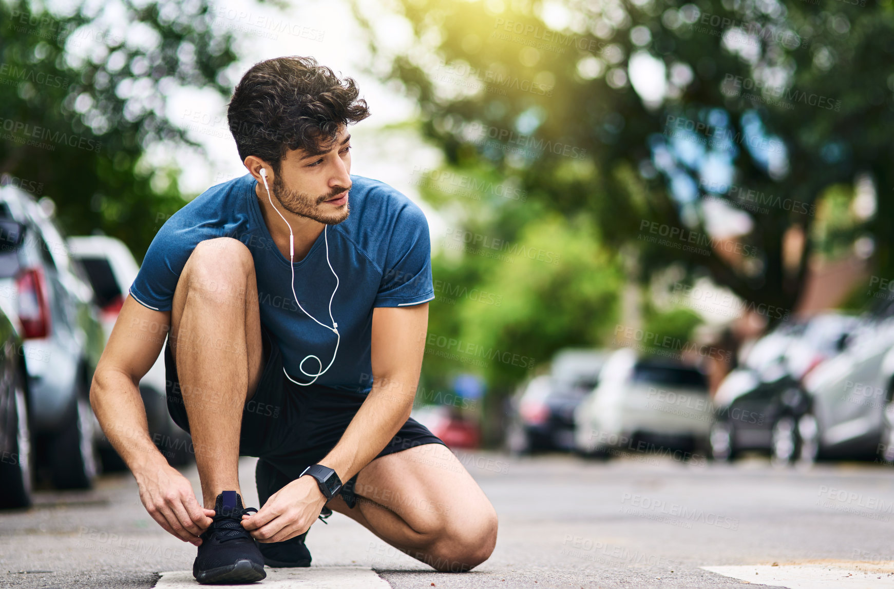 Buy stock photo Shot of a sporty young man tying his shoelaces while exercising outdoors