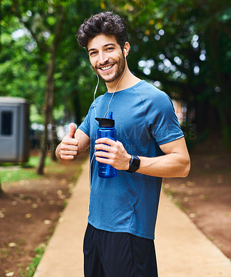 Buy stock photo Portrait of a sporty young man holding a water bottle and showing thumbs up while exercising outdoors