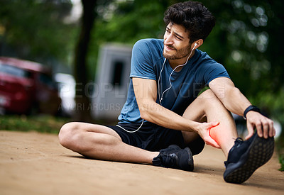 Buy stock photo Shot of a sporty young man holding his calf in pain while exercising outdoors