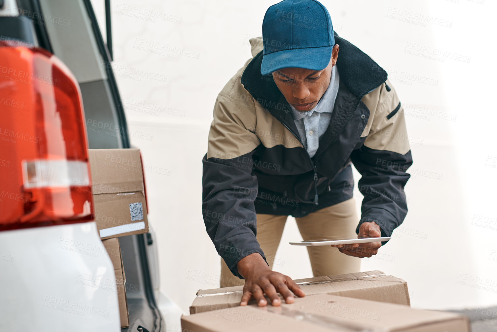 Buy stock photo Shot of a courier using a digital tablet while sorting boxes from a delivery van
