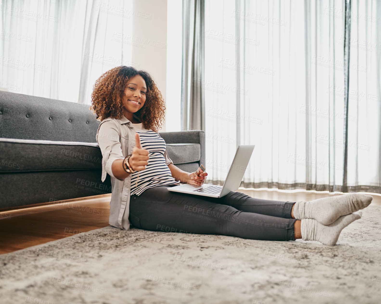 Buy stock photo Portrait of a cheerful young woman doing online shopping on her laptop while being seated on the floor at home