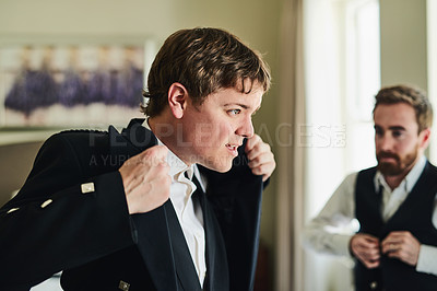 Buy stock photo Shot of a confident young man putting on a suit jacket while looking into a mirror to get ready for a wedding