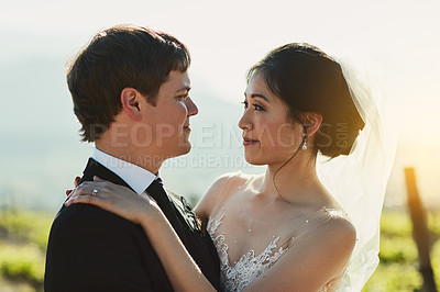 Buy stock photo Shot of a cheerful young bride and groom holding each other while looking eye to eye outside during the day