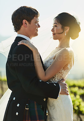 Buy stock photo Shot of a cheerful young bride and groom holding each other while looking eye to eye outside during the day