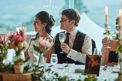 Buy stock photo Shot of a cheerful young bride and groom seated at a table together while holding champagne glasses for a celebratory toast