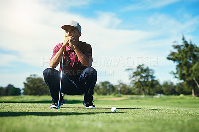Buy stock photo Shot of a focused young male golfer looking at a golf ball while being seated on the grass outside during the day