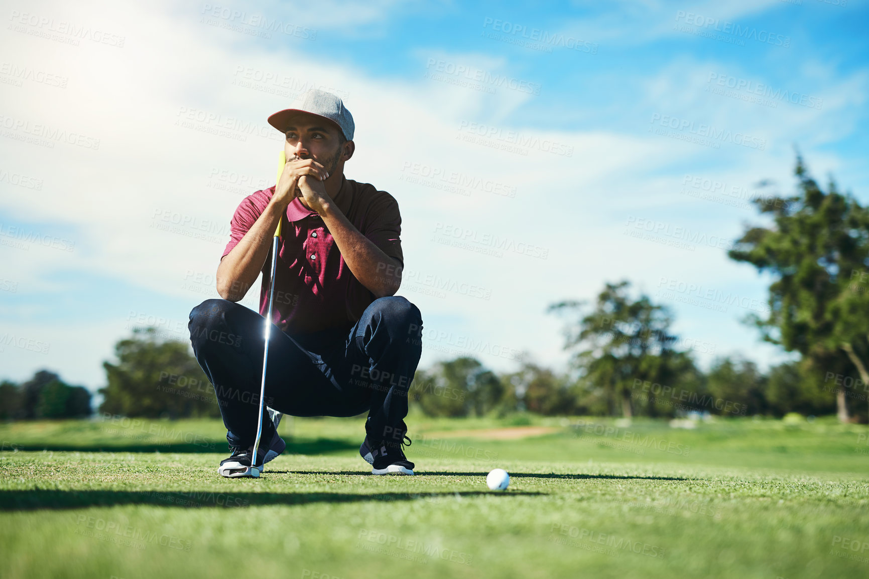 Buy stock photo Shot of a focused young male golfer looking at a golf ball while being seated on the grass outside during the day