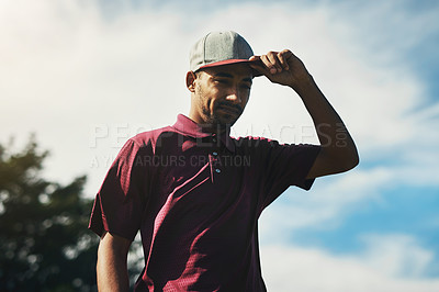 Buy stock photo Shot of a focused young male golfer holding his cap while looking at the ground outside on a golf course during the day
