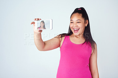 Buy stock photo Studio shot of a cute young girl taking a selfie with a mobile phone against a gray background