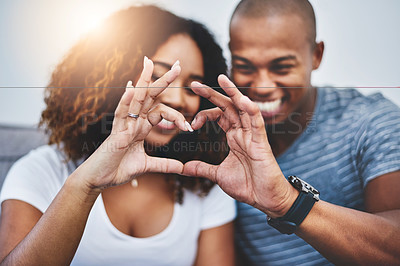 Buy stock photo Shot of a young couple making a heart shape with their fingers at home