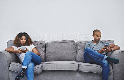 Buy stock photo Shot of a young couple texting on their cellphones at home