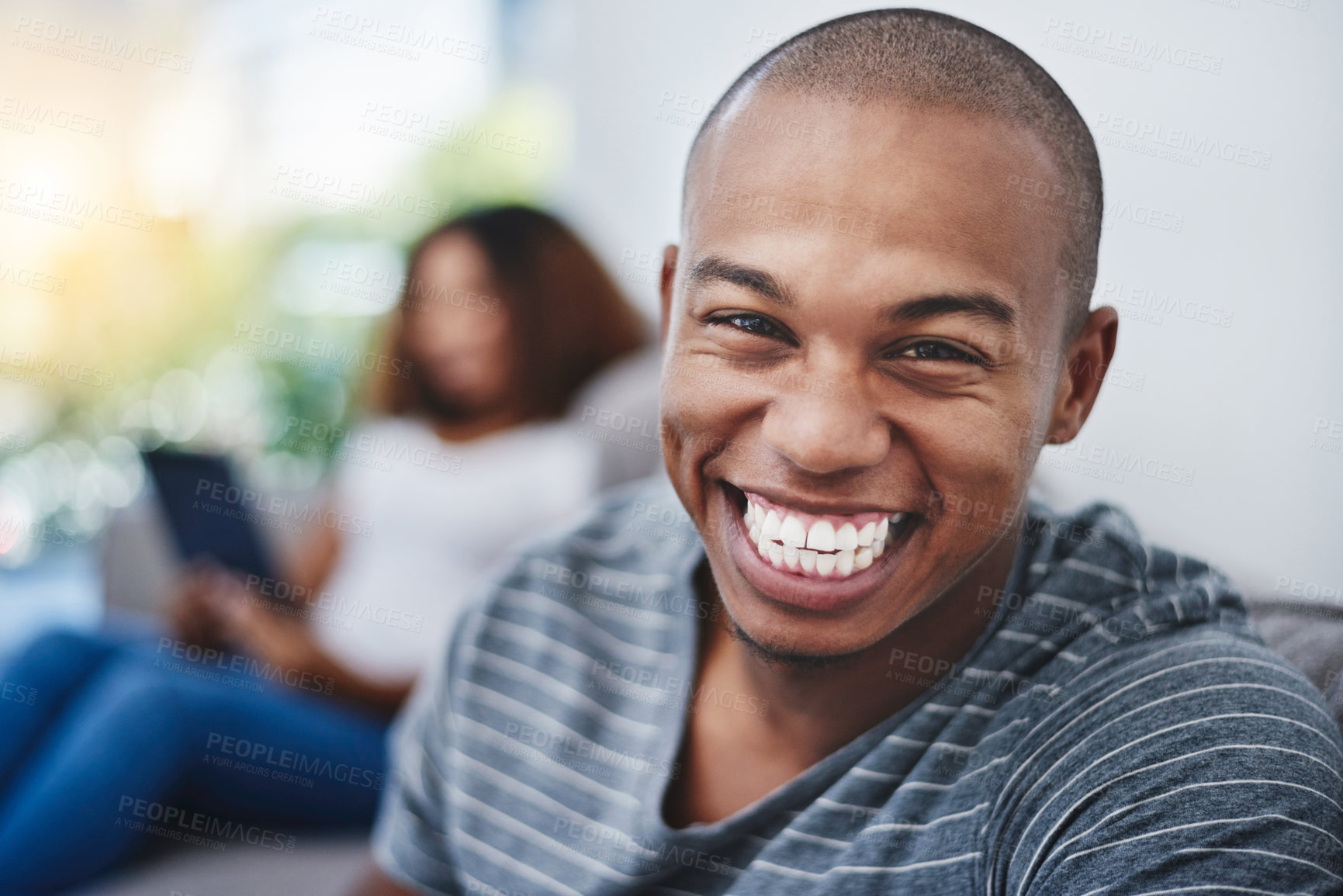 Buy stock photo Portrait of a young man relaxing at home with his girlfriend in the background