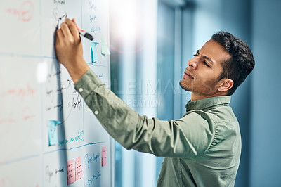 Buy stock photo Shot of a focused young businessman writing on a white while standing inside of the office during the day