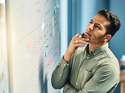 Buy stock photo Shot of a focused young businessman standing next to a white board while looking at it and contemplating inside of the office