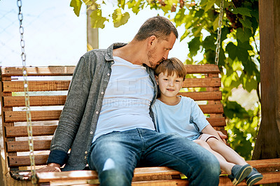 Buy stock photo Shot of a father and his adorable son relaxing together on a garden swing
