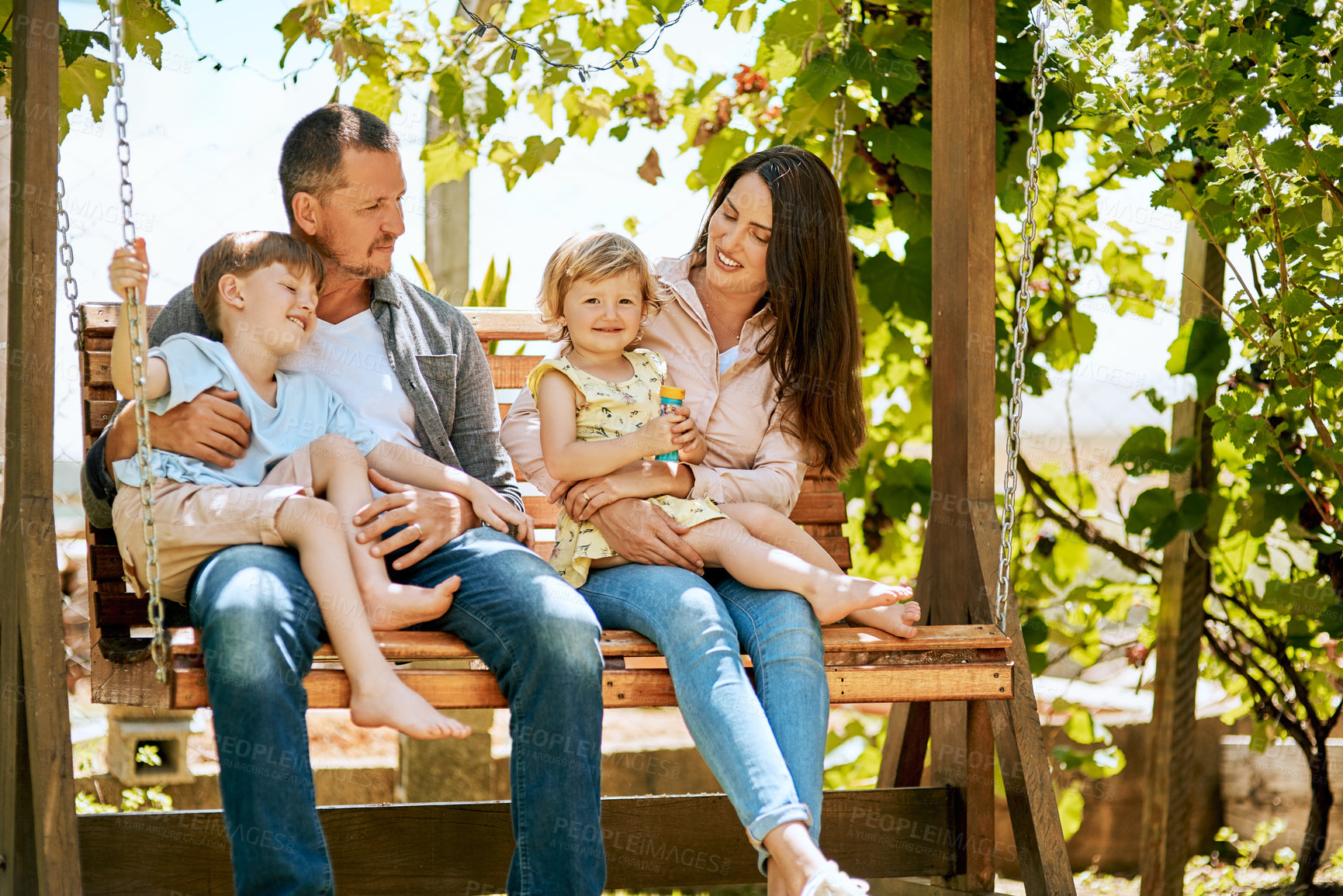 Buy stock photo Shot of a family of four relaxing together on a garden swing