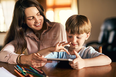 Buy stock photo Shot of a little boy using a digital tablet while doing homework with help from his mother