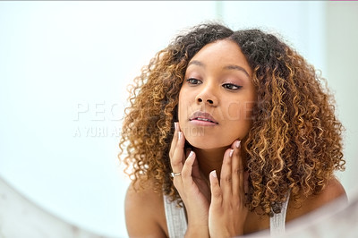 Buy stock photo Shot of a confident young woman holding her face while looking at herself in the mirror at home in the bathroom