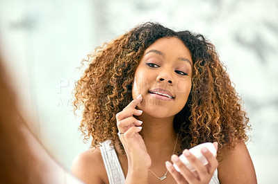 Buy stock photo Shot of a confident young woman applying skin cream on her face while looking into the mirror in the bathroom at home